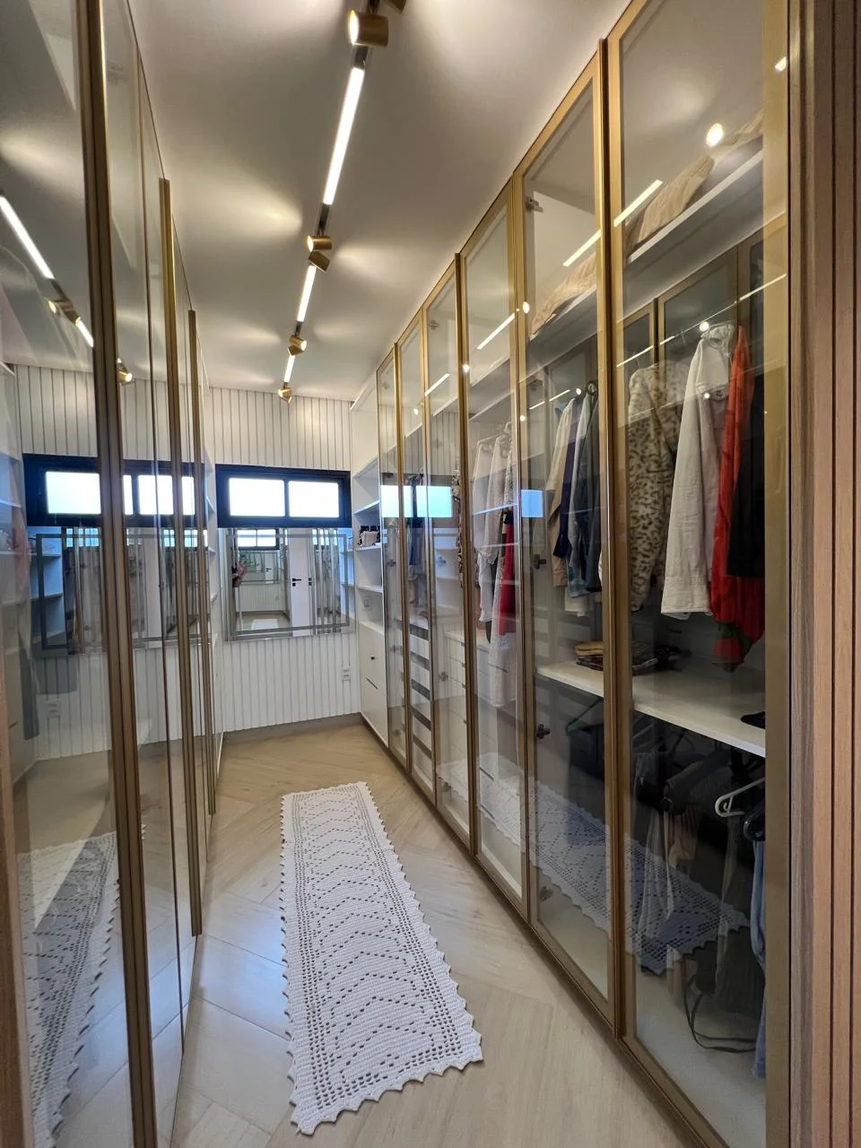 Closet amplo com portas de vidro reflecta, perfis em alumínio dourado e iluminação em LED interna