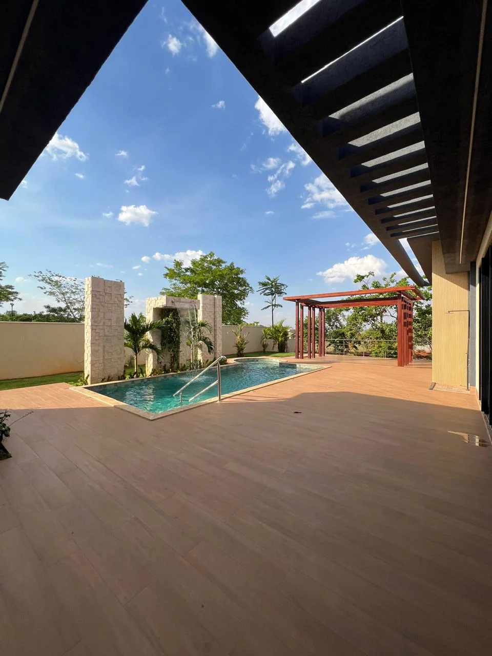 Piscina aquecida revestida em pastilhas com cascata em pedra natural e deck amadeirado na Casa Moderna Mobiliada do Condomínio Aldeia dos Sonhos