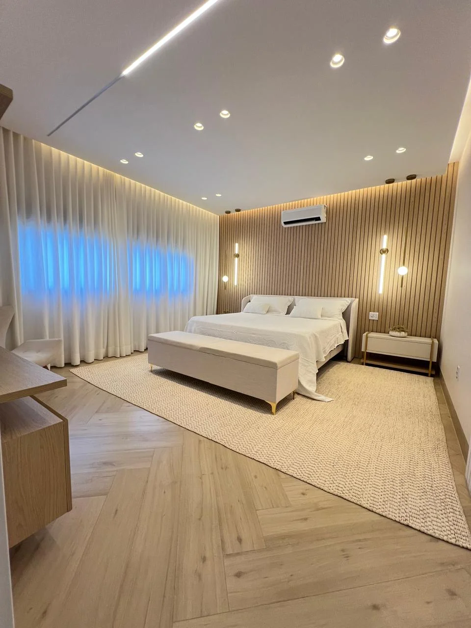 Suíte master do casal com cama king size, cabeceira ripada de madeira, iluminação indireta e ar-condicionado